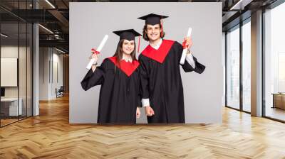 Young couple posing with their diplomas on white background Wall mural